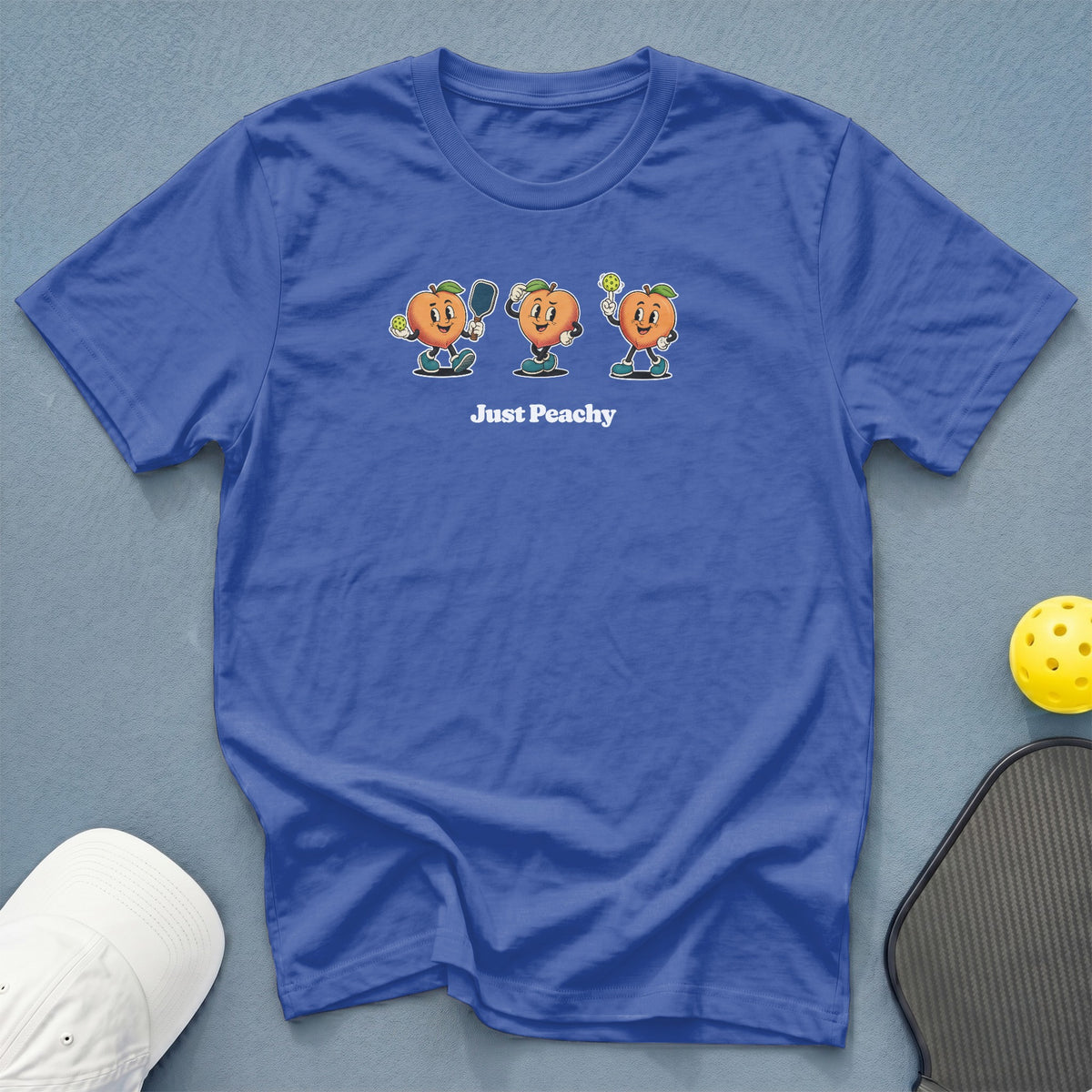 Blue t-shirt with cartoon peaches playing pickleball, text "Just Peachy".
