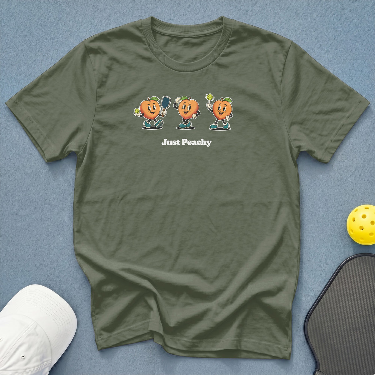 Olive green t-shirt with "Just Peachy" text and cartoon peaches playing pickleball.