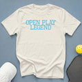 Cream t-shirt with blue text "OPEN PLAY LEGEND", pickleball paddle, and cap.