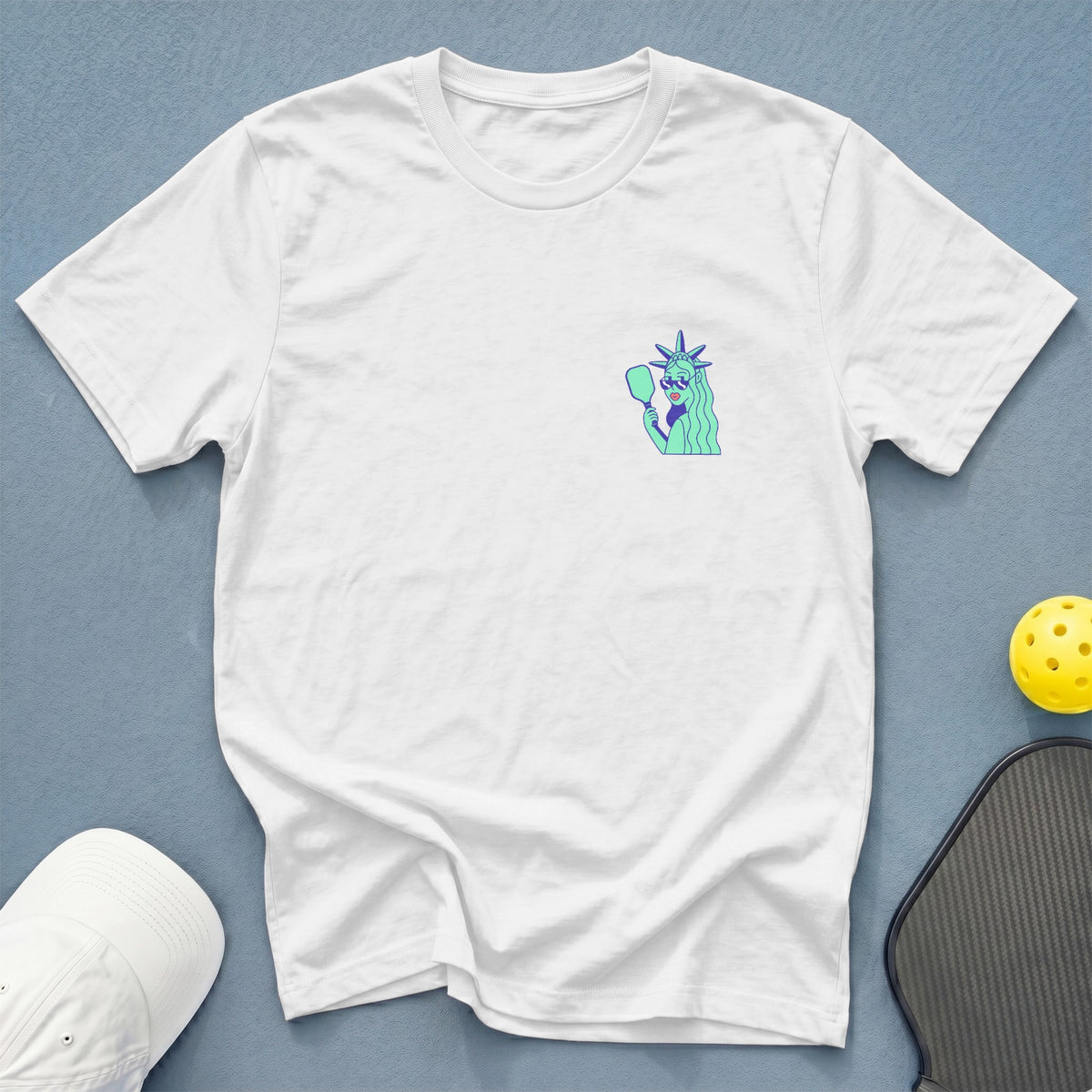 White t-shirt with a small graphic of the Statue of Liberty holding a pickleball paddle.
