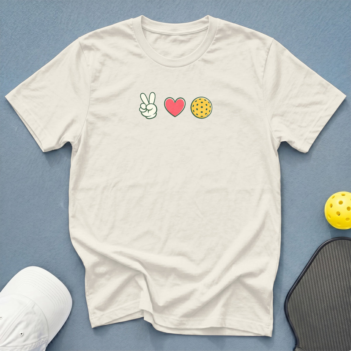 White t-shirt with peace, heart, and pickleball graphic; cap and paddle visible.