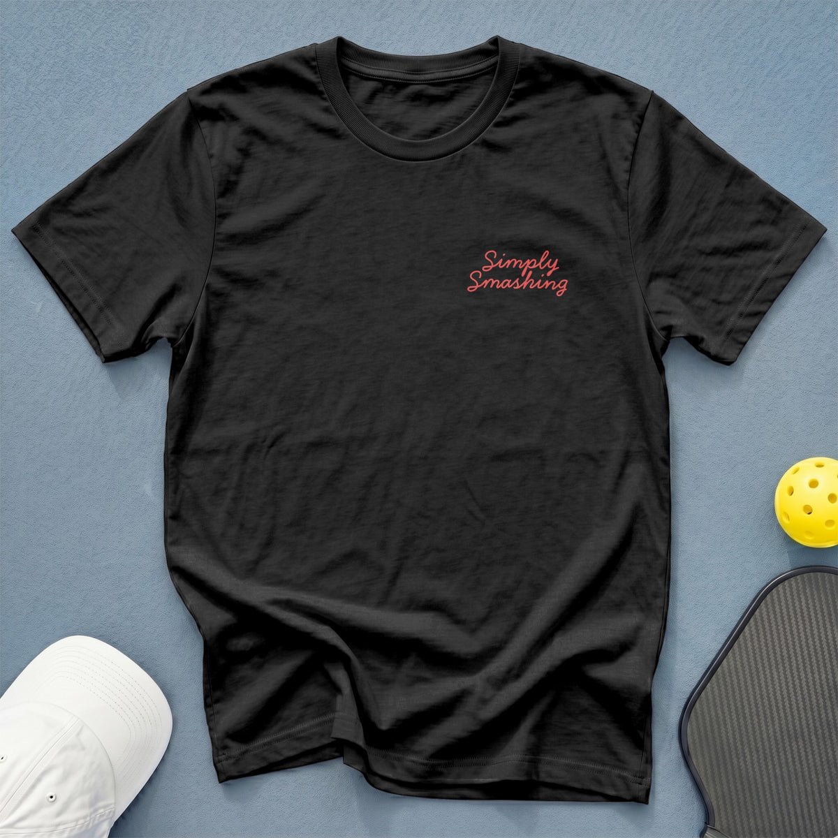 Black t-shirt with "Simply Smashing" text, pickleball paddle, ball, and hat.