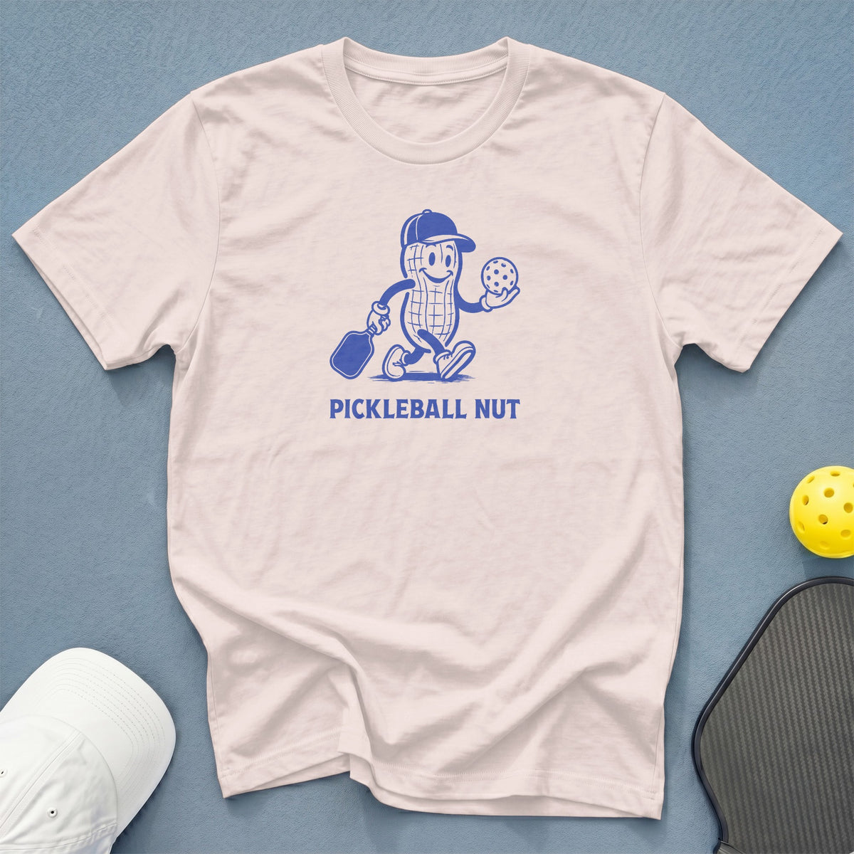 White t-shirt with blue graphic of a peanut character holding a pickleball and paddle.