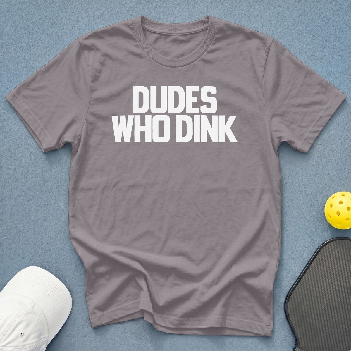 Gray t-shirt with white text "DUDE WHO DINK" next to pickleball gear.