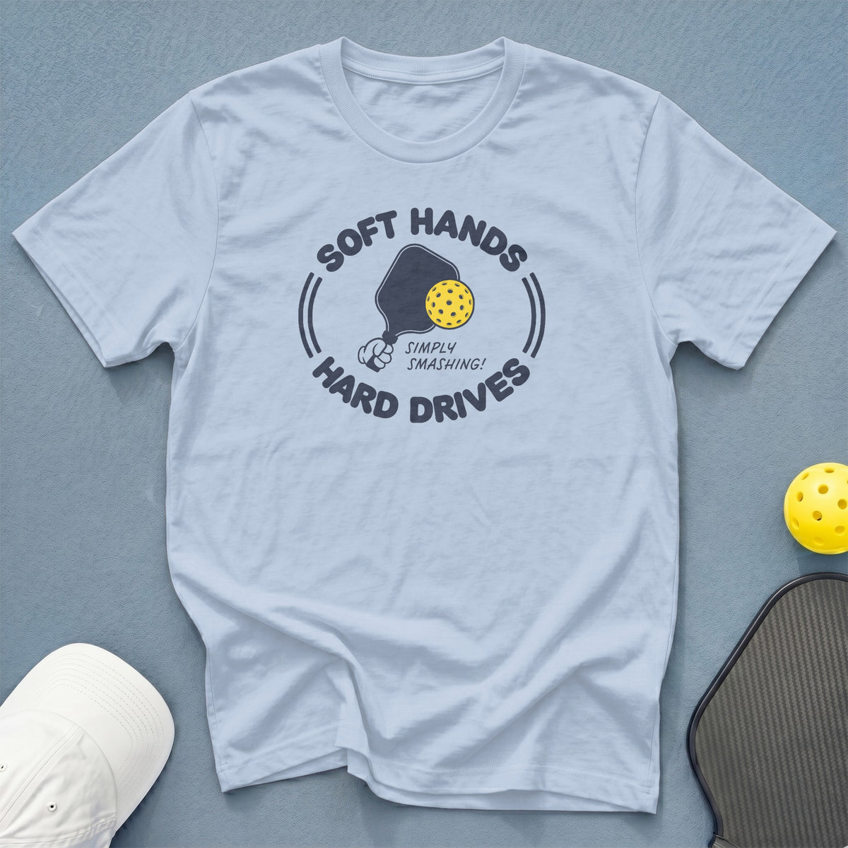 Light blue t-shirt with a graphic of a pickleball paddle and ball, reading "Soft Hands Hard Drives".
