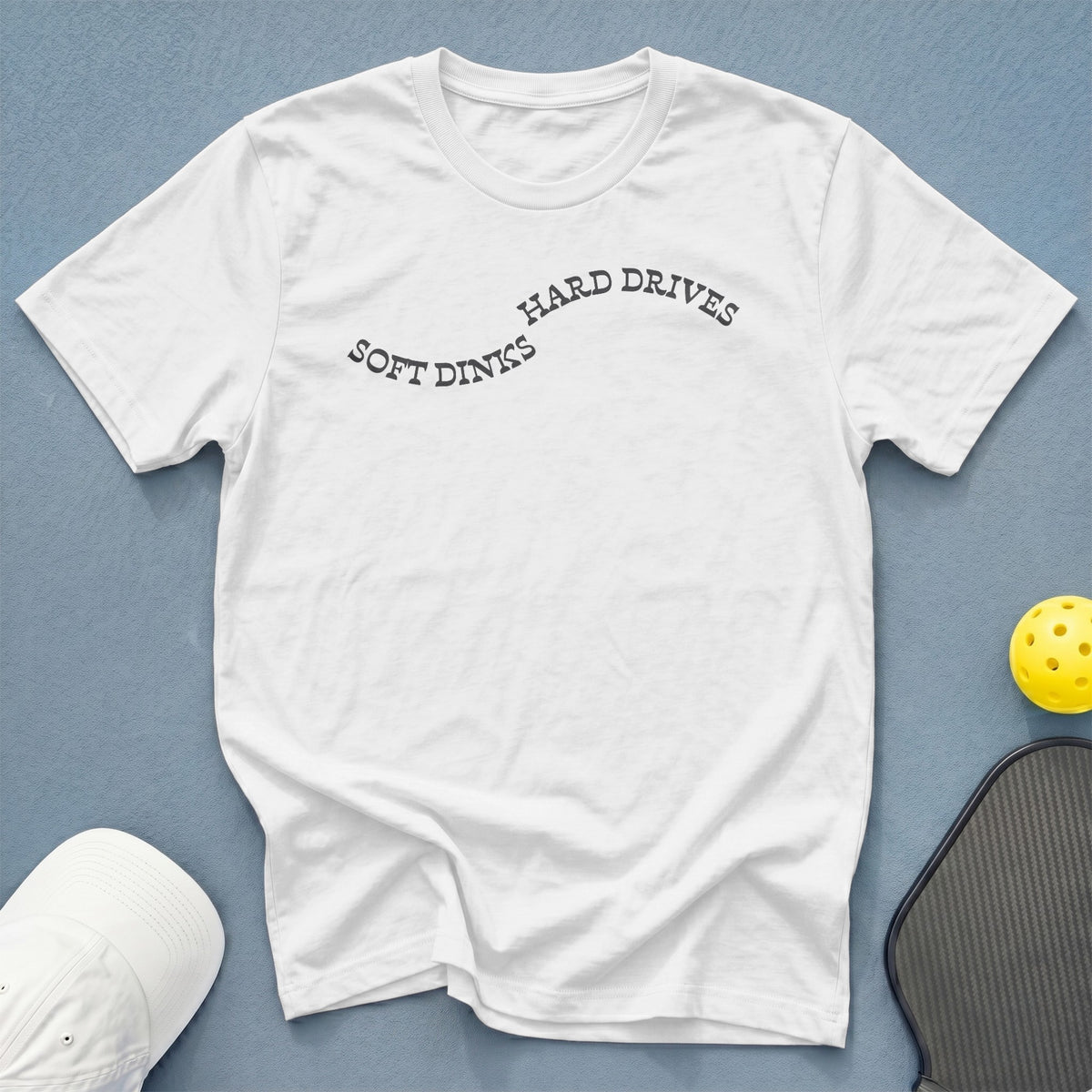 White t-shirt with "SOFT DINKS HARD DRIVES" text, pickleball paddle, and ball.