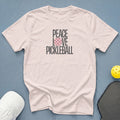Light pink t-shirt with "Peace Love Pickleball" graphic and pickleball accessories.