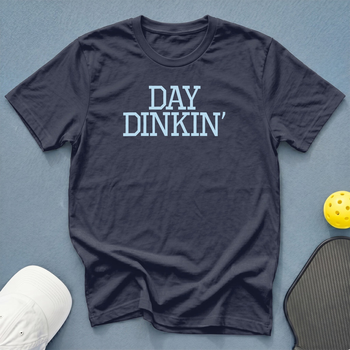Dark t-shirt with light blue text "DAY DINKIN'" and pickleball gear.