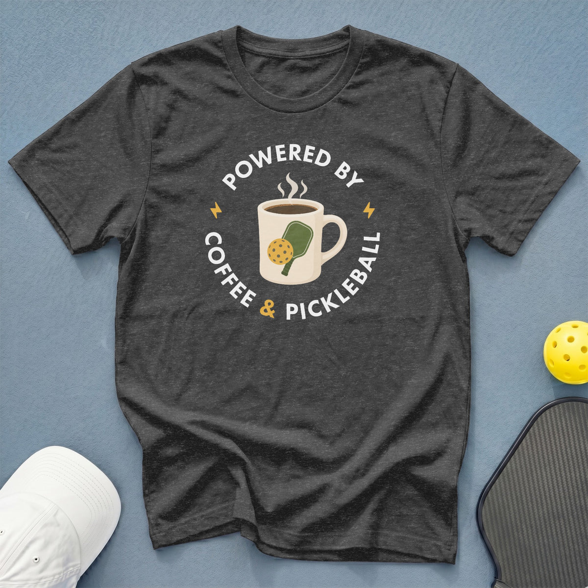 Dark t-shirt with "Powered by Coffee & Pickleball" graphic and pickleball accessories.
