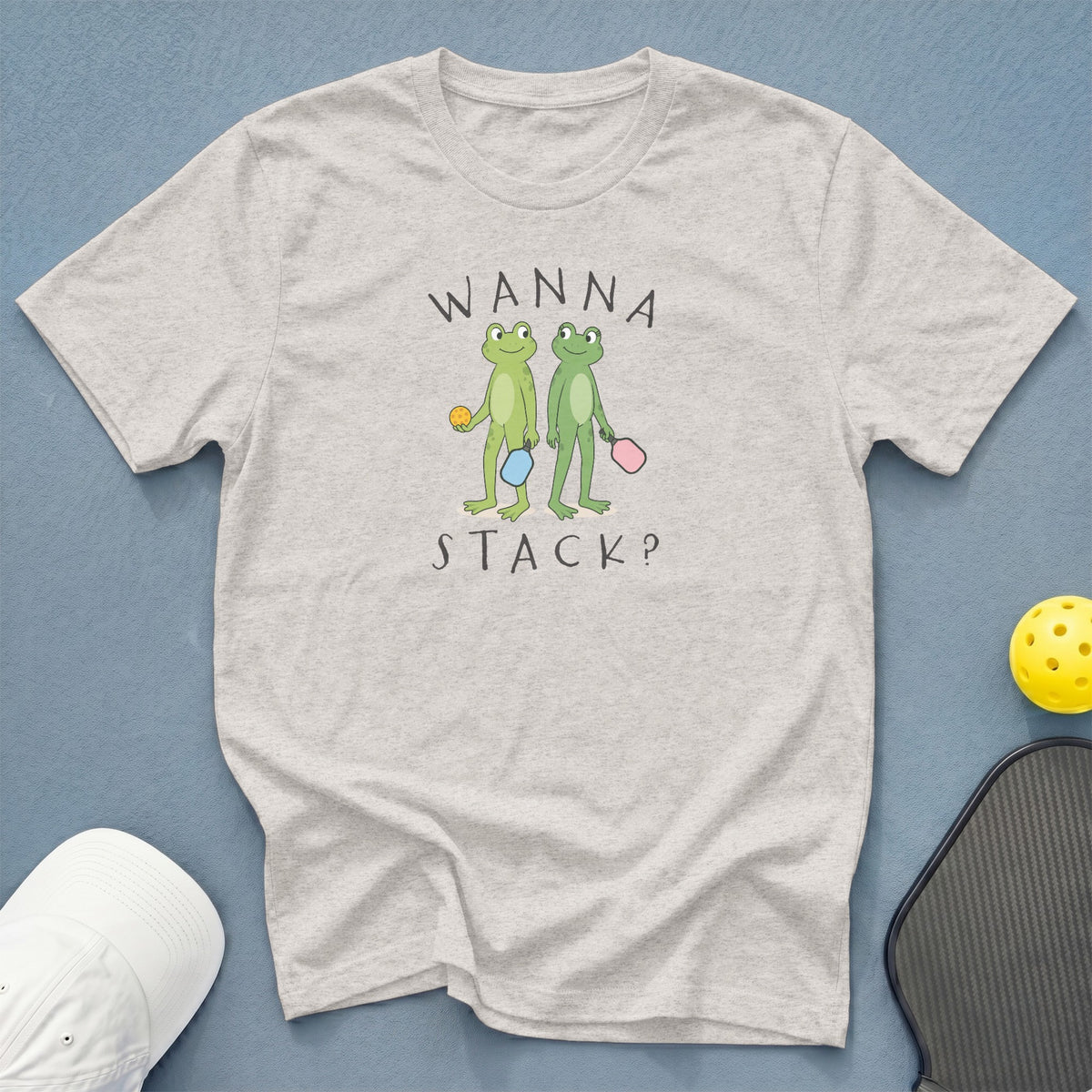 Light grey t-shirt with cartoon frogs holding pickleball paddles and ball, text "WANNA STACK?".