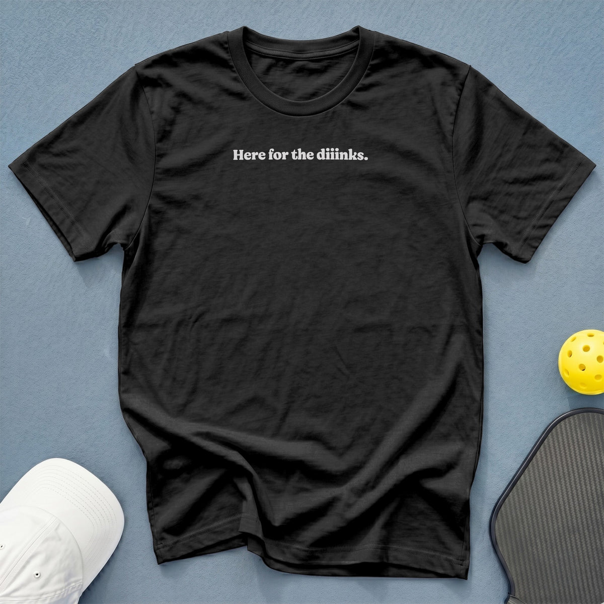 Black t-shirt with white text "Here for the diinks.", pickleball, and cap.