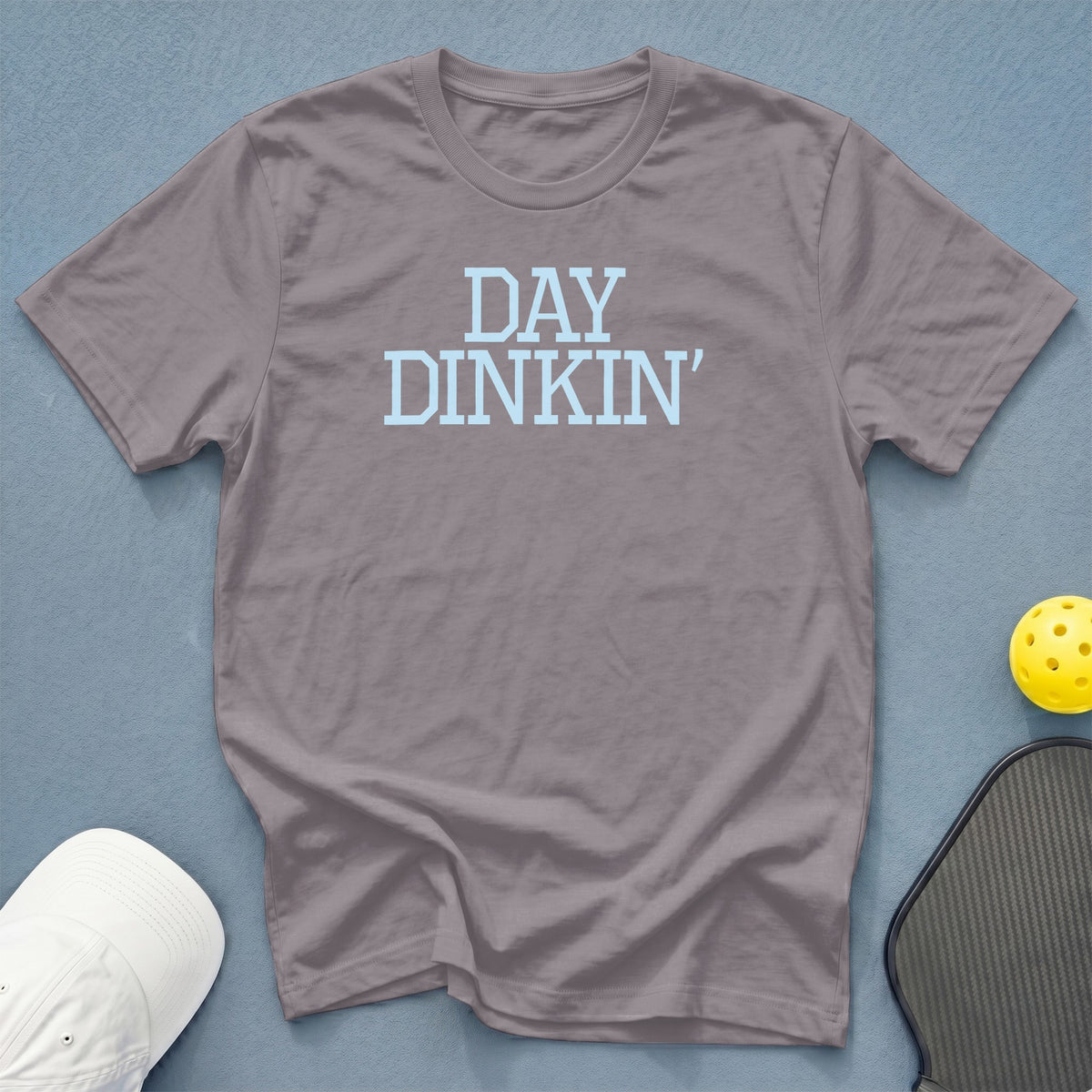 Gray t-shirt with "DAY DINKIN'" text, pickleball, and hat.