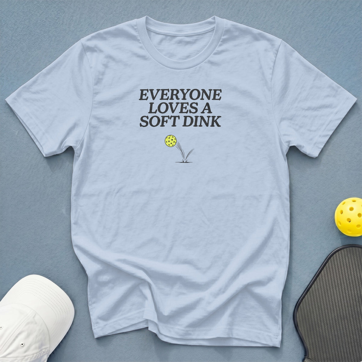 Light blue t-shirt with "EVERYONE LOVES A SOFT DINK" text and pickleball graphic.