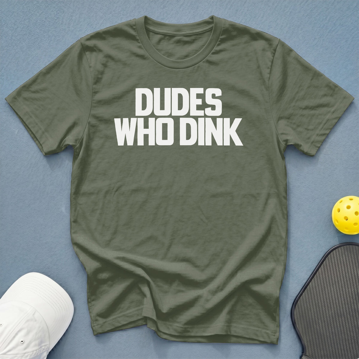 Olive green t-shirt with white text "DUDES WHO DINK", pickleball paddle and ball.
