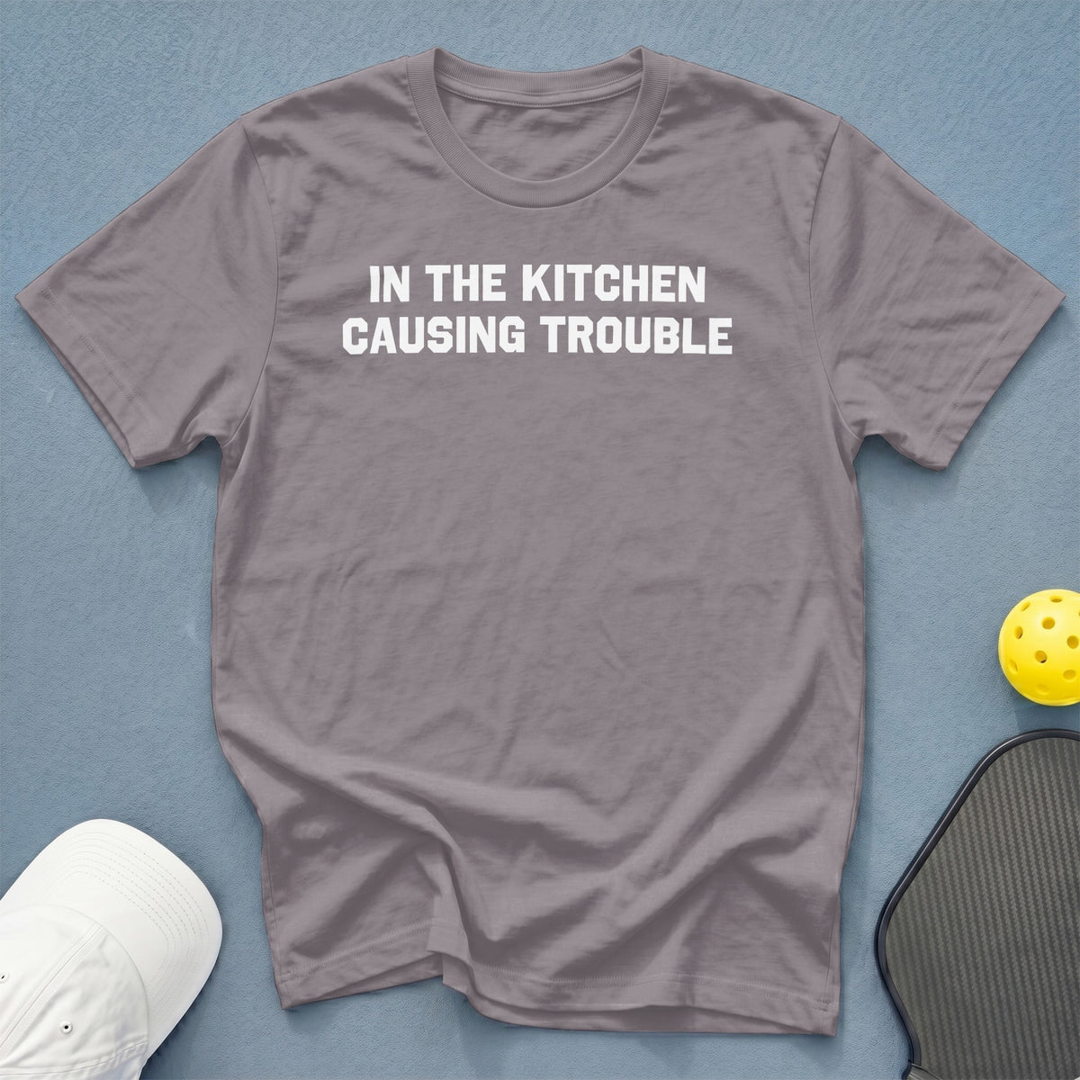 Grey t-shirt with white text "IN THE KITCHEN CAUSING TROUBLE"