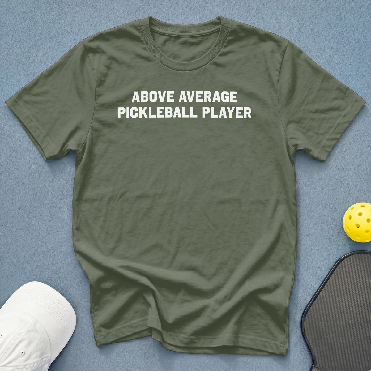 Olive green t-shirt with white text reading "ABOVE AVERAGE PICKLEBALL PLAYER".