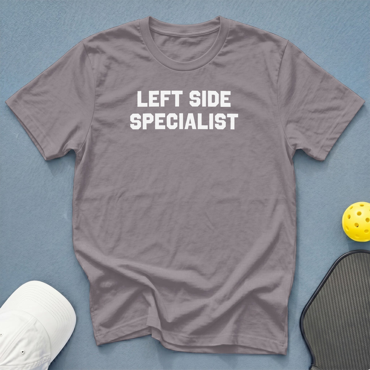 Gray t-shirt with "LEFT SIDE SPECIALIST" text, white hat, pickleball paddle, and yellow ball.