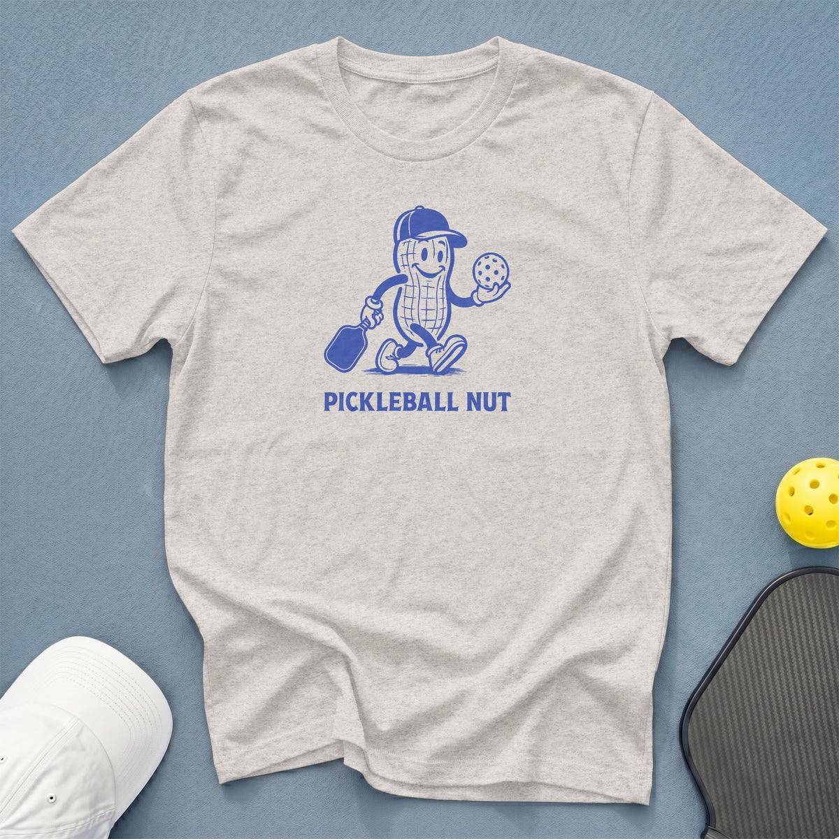 Light grey t-shirt with blue cartoon peanut holding pickleball and paddle, text "PICKLEBALL NUT".